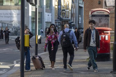 Londra, İngiltere, 2 Mayıs 2025. Londra 'nın merkezinde sokakta kırmızı bir telefon kulübesiyle yürüyen yayalar..