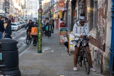 Londra, İngiltere, 2 Mayıs 2025. Bisikletiyle duran ve kaldırımda telefonunu kontrol eden genç bir kadın.