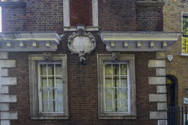 Londra, İngiltere, 2 Mayıs 2025. İki kuşak penceresi, dekoratif taştan bir plaket ve klasik beyaz taş quoins ve kornişlerden oluşan tarihi kırmızı tuğla bina cephesinin yakın çekimi..