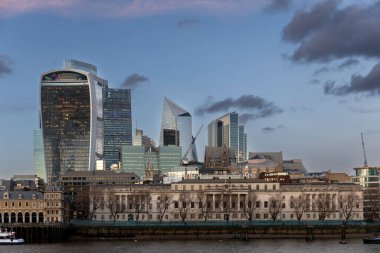 Londra, İngiltere, 2 Mayıs 2025. Alacakaranlıktaki zıt ufuk çizgisi, Thames boyunca uzanan nehir kenarındaki eski binaların klasik, uzun cephesinin arkasında yükselen finans bölgesinin modern, ayırt edici gökdelenlerinin yer aldığı..