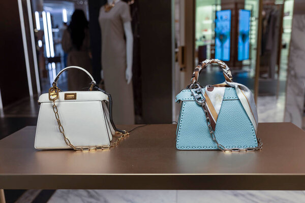 London, UK, 2 May, 2025. Harrods. Two luxury designer handbags, one cream and one mint green, are displayed on a gold-toned table in a brightly lit, upscale retail environment.