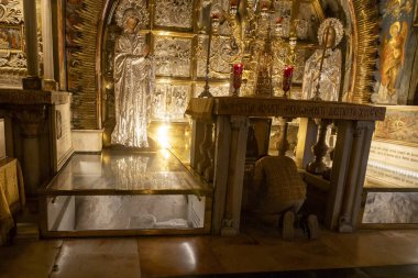 Kudüs, İsrail, 23 Ekim 2025, Kutsal Mezar Kilisesi. Bir hacı, cam kaplı kutsal bir taşın yanında, süslü bir sunağın altında diz çöker.,