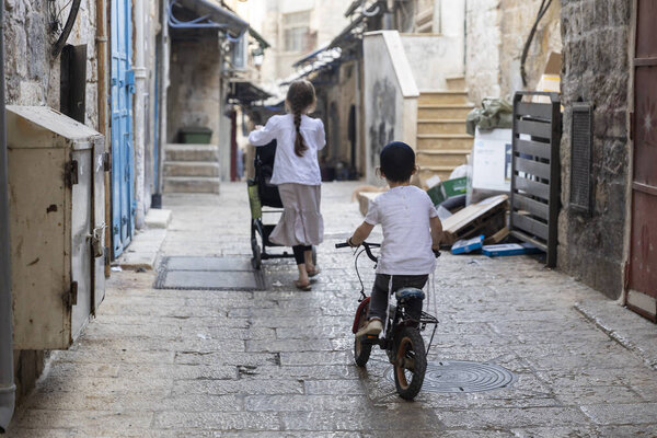 Jerusalem, Israel, 23 October 2025 A boy rides a small bicycle while an older girl pushes a stroller in a narrow, cobbled alleyway of the old city 