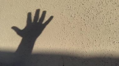 Bir elin gölgesi, pürüzlü sıva ve soyulmuş boyayla dokulu sarı bir duvara doğru hareket eder..