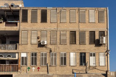İsrail 'in Tel Aviv kentindeki Kiryat Melacha sanatçılarının çeyreğindeki sıra sıra pencere panjurları ve klima ünitelerinin yer aldığı yıpranmış, çok katlı bir binanın ayrıntılı dış görünüşü açık mavi gökyüzüne karşı hazırlanıyor..