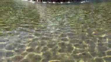 Güneş ışığı yansımaları çeşmede dans eder, güneşli bir günde parıldayan yansımalar ve çarpıtmalar yaratır..