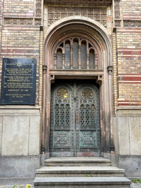 Berlin, Almanya, 2 Ekim 2025, bir sinagogun girişi geometrik desenli bronz kapılar ve granit basamakların üzerindeki tuğla cepheye bir hatıra plaketi. Oranienburger Strae 'deki Yeni Sinagog