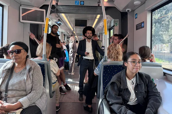 Kudüs, İsrail, 28 Ekim 2025, kalabalık, modern bir trenin içinde, merkezde ortodoks bir Yahudi de dahil olmak üzere çeşitli bir grup insan ayakta ve oturuyor..