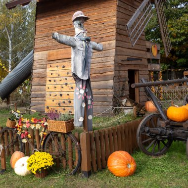 Tahta bir yel değirmeninin yanında duran korkuluk ve tırmanma duvarı, balkabakları, kasımpatılar ve bir bisiklet sepetinde heather ile çevrili.