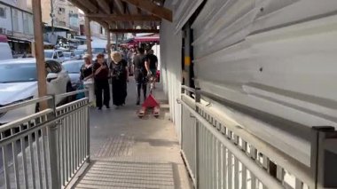 Hayfa, İsrail, 3 Kasım 2025, Talpiot Market 'te kadın müşteriler ona doğru yürürken bir adam arkasında bir platform tramvayı çekiyor..