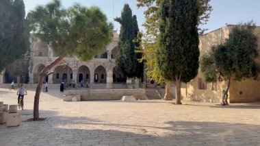 Kudüs, İsrail, 9 Ekim 2025, Beit Rothschild Evi yakınlarındaki meydanda bisiklet süren bir Ortodoks çocuk. Mahse Meydanı, kaldırımlı taş avluda tarihi bir binanın önünde tekrarlayan kemerler serisi var..