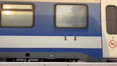 Hayfa, İsrail, 7 Kasım 2025, insanlar bitişikteki platformda bir bankta otururken mavi bir tren vagonu hızla hareket ediyor..