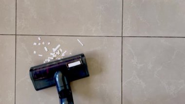 Elektrik süpürgesi açık bej kaplamalı mutfak zeminine saçılmış beyaz kağıt kırıntılarını temizliyor..