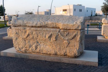 Ashkelon, İsrail, 20 Kasım 2025: Batan güneşin sıcak ışığıyla aydınlatılan çiçek ve asma motifleri içeren antik bir kireç taşı lahitinin yan görüntüsü.