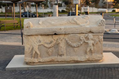 Ashkelon, İsrail, 20 Kasım 2025: Kapağında yaslanmış bir figür ve oyulmuş yardım panelleri bulunan çok detaylı antik lahit, Putti 'nin elinde bir çelenk tutması gibi figürler tasvir ediyor..