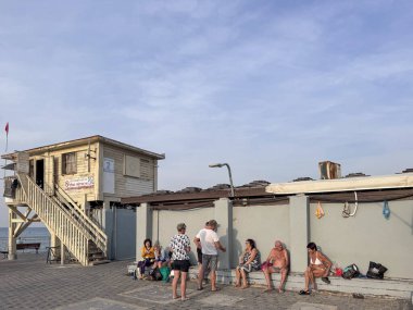 Hayfa, İsrail, 3 Aralık 2025, güneşli bir günde bir plaj cankurtaran istasyonunda dinlenen ve oturan bir grup insan.