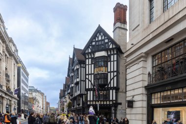 Londra, İngiltere, 6 Aralık 2025, Londra 'nın ikonik siyah-beyaz sahte Tudor cephesi, kalabalık bir caddeden geçen bulutlu bir gökyüzü..