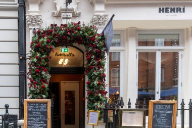 Londra, İngiltere, 6 Aralık 2025, Henrietta restoranının girişi, geleneksel karatahta menüleri çerçeveli, yemyeşil bir çelenk ve koyu kırmızı kadife fiyonklarla süslenmiş..