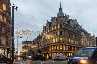 Londra, İngiltere, 7 Aralık 2025, Sloane Caddesi 'nin alacakaranlıkta geniş bir görüntüsü, köşedeki Burberry mağazasını gösteriyor ve sokağın üstünde bayram tarzı yılbaşı ışıkları asılı..
