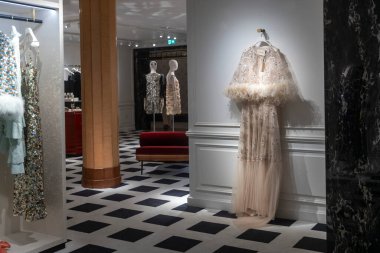 Londra, İngiltere, 7 Aralık 2025 'te siyah ve beyaz kareli döşeme ve altın sütunların yer aldığı üst düzey bir butiğin içindeki beyaz bir duvara tüylü pelerinli lüks bir gece elbisesi asıldı. Harrods Mağazası