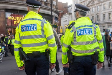 Londra, İngiltere, 13 Aralık 2025, iki metropoliten polis memurunun dikiz görüntüsü, şehir caddesinde yürüyen üniformalı iki polis memuru, ekipman kemerlerini gösteriyor..