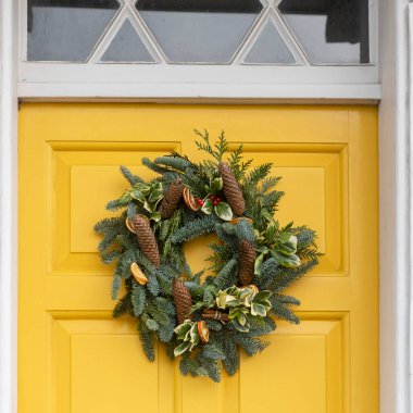 Çam kozalaklı Noel çelengi, kurutulmuş portakal dilimleri, sarmaşık ve çoban üzümleri parlak sarı ön kapıda asılı..