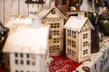 Kırsal, sıkıntılı, beyaz metal ev şekilli mum tutucular veya bir markette kırmızı beyaz desenli kumaş üzerinde satılığa çıkarılan dekoratif minyatür binalar..