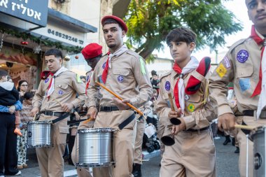 Hayfa, İsrail, 20 Aralık 2025, Noel keşif geçidi, kırmızı bereli bir grup genç izci bir tatil alayında davul ve çan çalıyorlar..