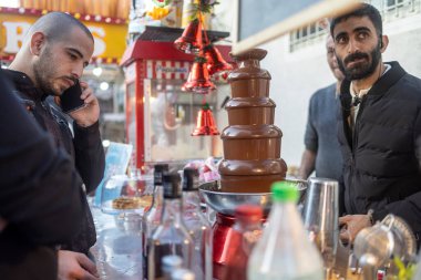 Hayfa, İsrail, 20 Aralık 2025 'te, bir adam akıllı bir telefonla konuşuyor. Bir çikolata şelalesinin yanında, sokak yemeklerinin olduğu yerde..