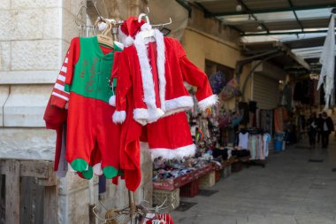 Nasıra, İsrail, 24 Aralık 2025 Kızıl Noel Baba, İsrail 'in eski Nasıra şehrindeki bir sokak pazarında satılık bir askıda asılı duran bebek ve bebekler için kostümler.