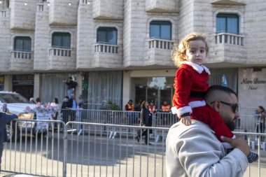 Nasıra, İsrail, 24 Aralık 2025 Noel Baba kostümü giymiş küçük bir çocuk babasının omuzlarında oturmuş Nasıra 'daki Noel geçit törenini izliyor.