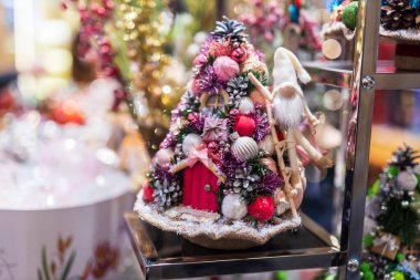 Minyatür bir Noel ağacı süslemesinde merdivene tırmanan sevimli pembe bir cüce süsü. Çam kozalakları ve toplarla pembe ve beyaz temalı bayram dekoru.