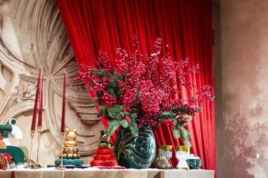 Yeşil vazoda kırmızı böğürtlenler ve kırmızı perdeye karşı altın tutacaklarda uzun kırmızı mumlar olan bir şenlik düzeninin yakın çekimi.