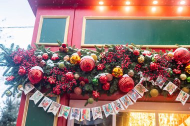 Köknar dalları, kırmızı böğürtlenler, süsler ve kartpostallarla süslenmiş Noel marketi cephesi;