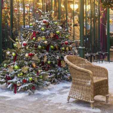 Açık hava kafe köşesi, karla kaplı Noel ağaçları hasır sandalyenin yanında yeşil ve kırmızı mücevherlerle süslenmiş.,