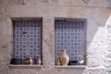 Taş bir iç mekanda dekoratif duvar oyukları mavi geometrik kiremit deseni ve raflarda küçük vintage nesneler