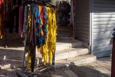 Renkli eşarplar ve tekstil taş basamakların ve kapalı metal kepenklerin yanındaki bir mağazanın önündeki askıda asılı.