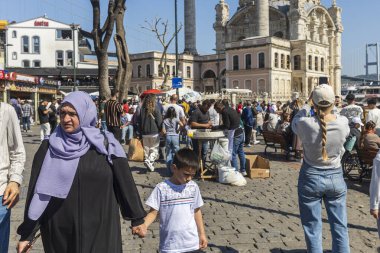 İstanbul, Türkiye, 5 Mayıs 2025, İstanbul, Türkiye 'de kalabalık kent meydanı, türban takan kadınlar da dahil olmak üzere çok sayıda insan yürüyor ve oturuyor. Başörtülü bir anne oğluna yol gösterir.