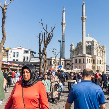İstanbul, Türkiye, 5 Mayıs 2025, Ortakoy Camii ve Boğaz Köprüsü yakınlarındaki yoğun meydanda yürüyen turuncu bluzlu kadın