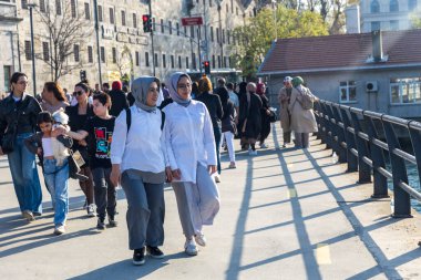 İstanbul, Türkiye, 5 Mayıs 2025, türbanlı iki kadın taş binalar, trafik ışıkları, kalabalık yakınlarındaki rıhtımda el ele tutuşuyor
