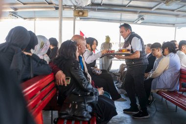 İstanbul, Türkiye, 5 Mayıs 2025, Garson İstanbul feribot güvertesi kırmızı banklarındaki yolculara yiyecek servisi yapıyor