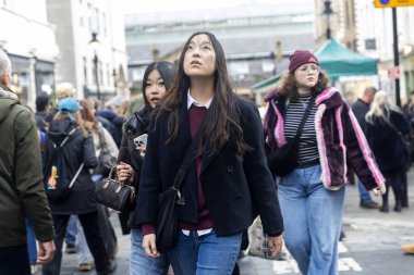 Londra, İngiltere, 7 Aralık 2025, Londra 'nın işlek bir alışveriş bölgesindeki mimariye bakan genç bayan turistlerin gizli çekimleri