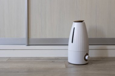 Modern beyaz ultrasonik hava nemlendirici. Oturma odasındaki gardırobun yanındaki açık ahşap zeminde duruyor.
