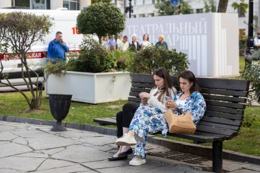 Moskova, Rusya, 17 Temmuz 2025 Halka açık bir parkta ahşap bir bankta oturan iki genç kadın, Moskova 'da bir yaz günü akıllı telefonlarına bakıyorlar.