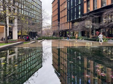 Londra, İngiltere, 5 Aralık 2025, Modern Kentsel Gelişim Bölgesi Kings Cross Londra Çağdaş cam tuğla ofis binaları çıplak ağaçlar bulutlu gökyüzü şarapları yansıtan havuz suyu