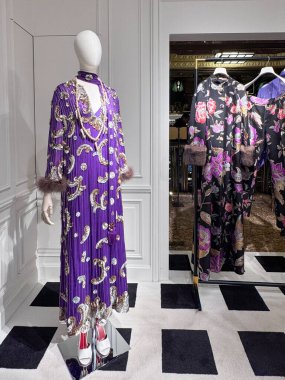 Londra, İngiltere, 5 Aralık 2025, lüks moda vitrininde beyaz manken özenle hazırlanmış mor menekşe işlemeli altın işlemeli gümüş süslemeli elbise kürk manşetli kırmızı botlar Valentino butiku.