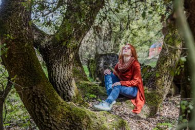Hayalperest kızıl saçlı kadın, kalın bir ağaç dalında oturmuş gökyüzüne bakıyor.