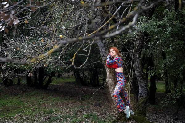 Parlak hippi kıyafetli kızıl saçlı bir kadının ağaçtan çekilmiş uzun bir resmi..