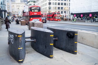 Londra, İngiltere, 2 Aralık 2025, Siyah metal güvenlik bariyerleri kaldırımda arka planda kırmızı çift katlı otobüsler