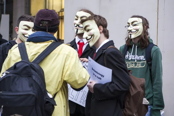 一名抗议者戴着盖伊面具拿著海报"山达基税" — 图库照片